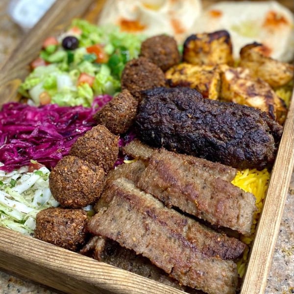 A wooden tray filled with Killer Kabab's falafel, chicken, beef, and lamb kebabs, with rice, salad, and hummus.