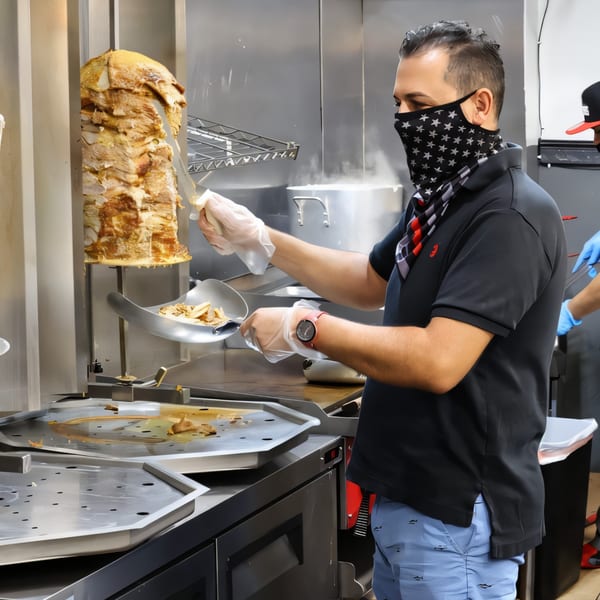 A Killer Kabab chef in a star-patterned mask shaves meat from a large vertical rotisserie.