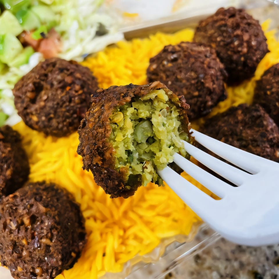 A Killer Kabab falafel, broken open on a fork, revealing its green interior, with yellow rice and salad.
