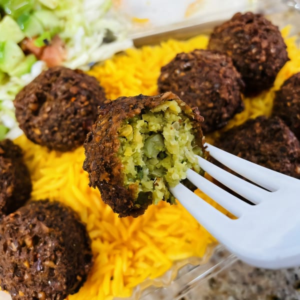 A Killer Kabab falafel, broken open on a white fork, revealing its green interior, with yellow rice.