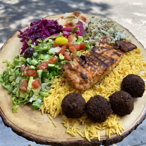 Killer Kabab platter with grilled salmon, falafel, rice, salad, hummus, and pickled vegetables on a wooden board.