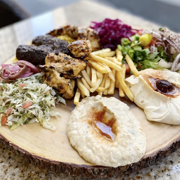A Killer Kabab platter with grilled chicken, beef kofta, fries, hummus, and salads on a wooden board.