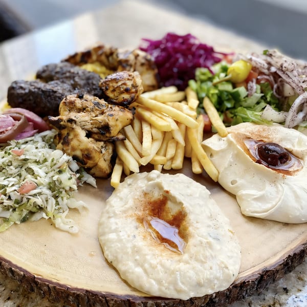 Killer Kabab platter with grilled chicken, kofta, fries, hummus, and salads on a wooden board.
