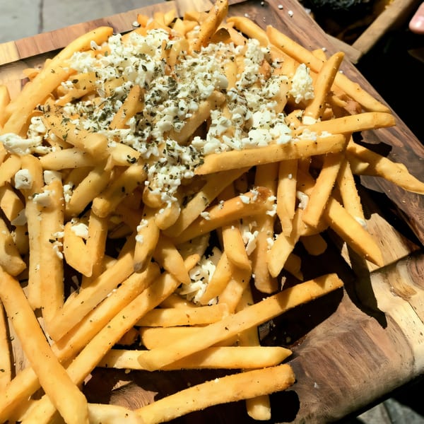 Golden french fries topped with crumbled feta cheese and dried herbs on a wooden board.