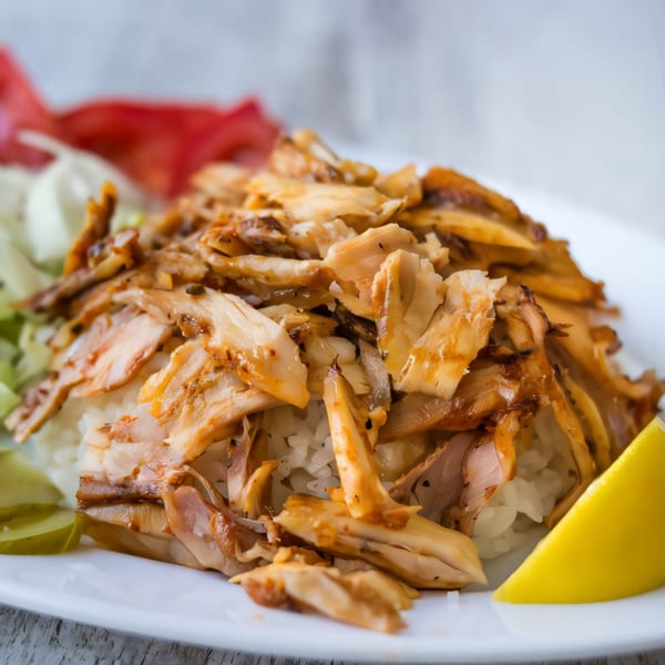 Killer Kabab's chicken kebab over rice with a lemon wedge and salad on a white plate.